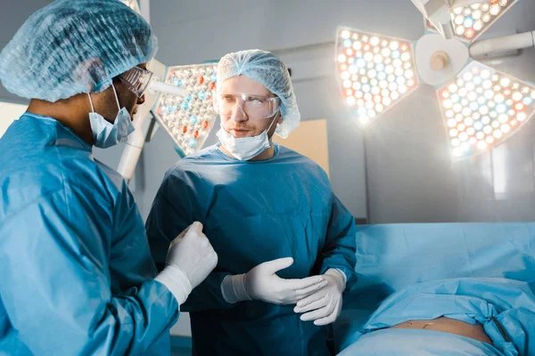 Infermiere e chirurgo in uniforme e maschere mediche che parlano in sala operatoria — Foto stock