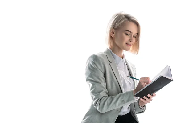 Alegre, atractiva empresaria con pelo rubio escribiendo en cuaderno aislado en blanco - foto de stock