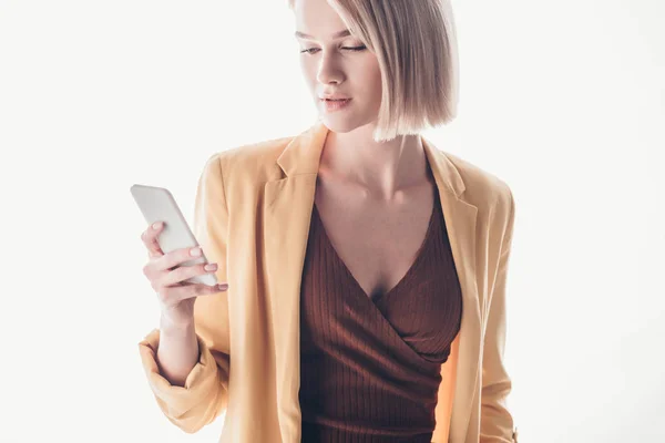 Mujer rubia reflexiva y atractiva usando el teléfono inteligente en gris - foto de stock