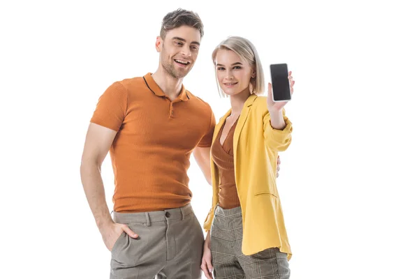 Sonriente mujer bonita mostrando teléfono inteligente con pantalla en blanco, mientras que de pie cerca de hombre guapo aislado en blanco - foto de stock