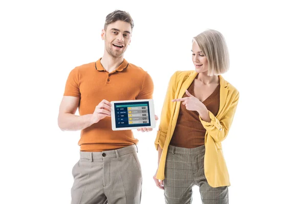 Homem sorrindo segurando tablet digital com sportbets app na tela perto de mulher bonita apontando com o dedo isolado no branco — Fotografia de Stock