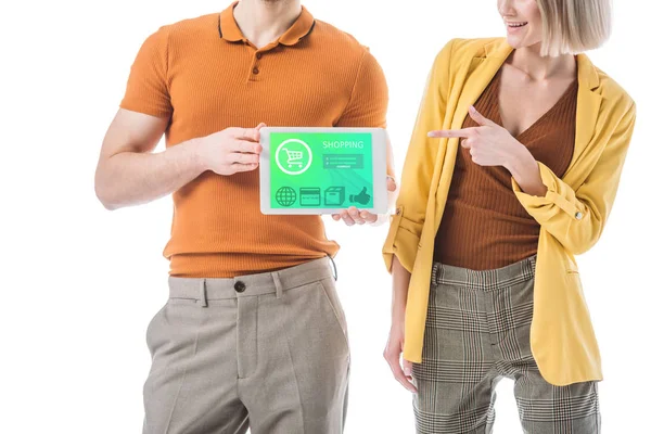 Vista parcial del hombre sosteniendo la tableta digital con la aplicación de compras en la pantalla, mientras que de pie cerca de la mujer señalando con el dedo aislado en blanco - foto de stock