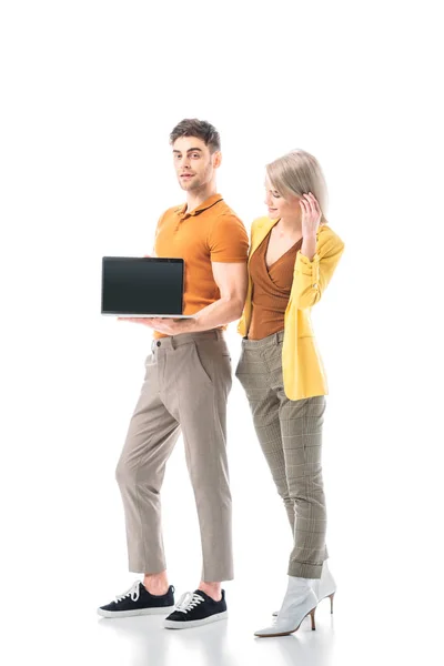 Hombre guapo sosteniendo portátil con pantalla en blanco, mientras que de pie cerca de la mujer bonita aislado en blanco - foto de stock
