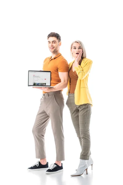 Улыбающийся мужчина держит ноутбук с airbnb веб-сайт на экране, стоя рядом удивленный женщина изолированы на белом — стоковое фото