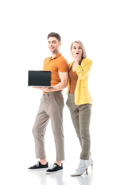 Schöner lächelnder Mann mit Laptop und leerem Bildschirm, während er in der Nähe einer ziemlich überraschten Frau steht, die auf weiß isoliert ist — Stockfoto