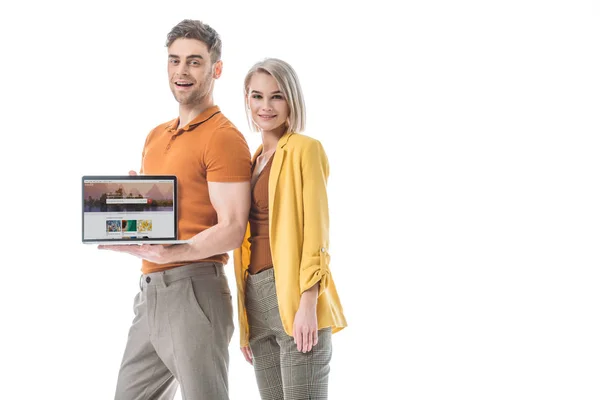 Hombre sonriente de buen aspecto sosteniendo el ordenador portátil con obturador sitio web en la pantalla, mientras que de pie cerca de la hermosa mujer aislada en blanco - foto de stock