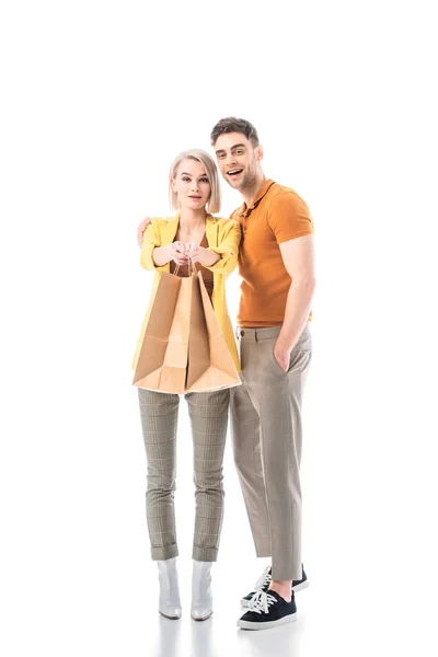 Beautiful blonde woman holding paper bags while standing near handsome man and looking at camera isolated on white — Stock Photo