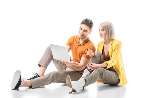 Hombre guapo sonriente con el ordenador portátil y la mujer bonita con tarjeta de crédito sentado en blanco - foto de stock
