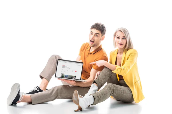 Homme excité tenant ordinateur portable avec airbnb site à l'écran tout en étant assis près de femme surprise sur blanc — Photo de stock