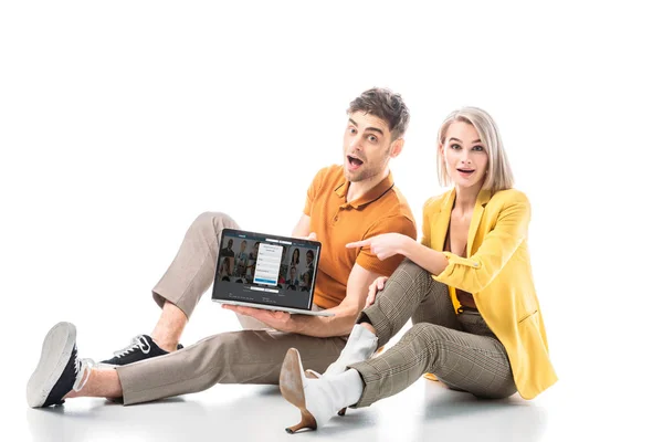 Красивый возбужденный мужчина держит ноутбук с веб-сайтом linkedin на экране, сидя рядом с симпатичной женщиной в белом — стоковое фото