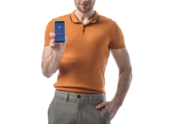 Vista parcial del hombre con la mano en el bolsillo celebración de teléfono inteligente con aplicación de Facebook en la pantalla aislada en blanco - foto de stock