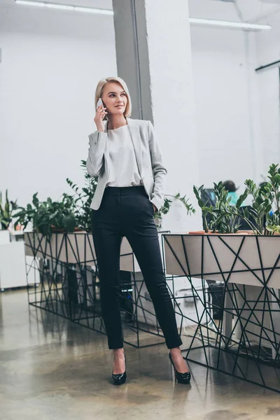 Schöne blonde Geschäftsfrau, die im Büro auf dem Smartphone spricht — Stockfoto