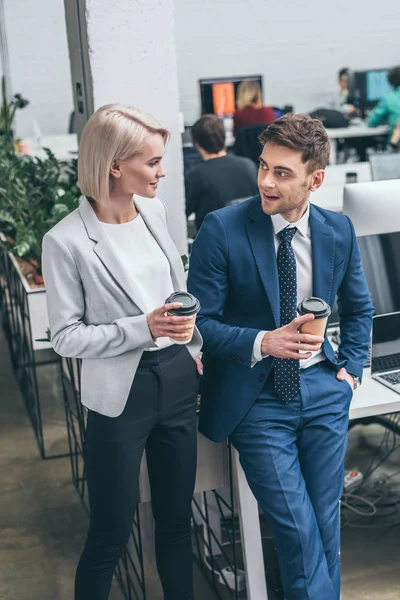 Pretty businesswoman and handsome businessman holding paper cups and talking in offce — Stock Photo