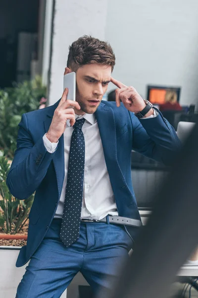 Selektiver Fokus des nachdenklichen Geschäftsmannes, der im Büro auf dem Smartphone spricht — Stockfoto
