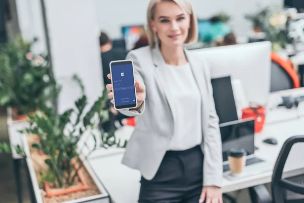 Selektiver Fokus der hübschen Geschäftsfrau mit Smartphone und Facebook-App auf dem Bildschirm — Stockfoto