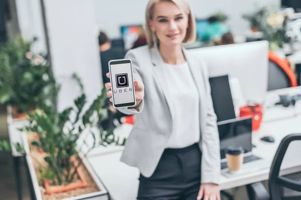Selective focus of smiling businesswoman holding smartphone with uber app on screen — Stock Photo