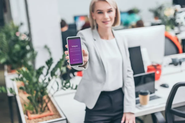 Attraktive Geschäftsfrau hält Smartphone mit Instagram-App auf dem Bildschirm — Stockfoto
