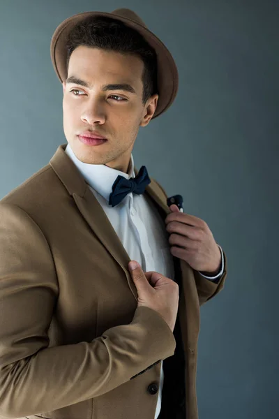 Stylish mixed race man in suit and hat posing isolated on grey — Stock Photo