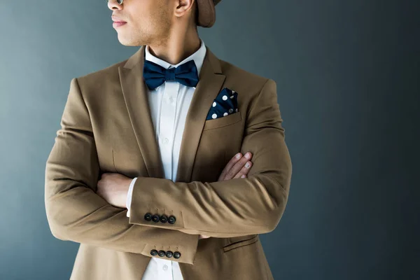 Vue recadrée de élégant homme de race mixte en costume avec les bras croisés isolés sur gris — Photo de stock