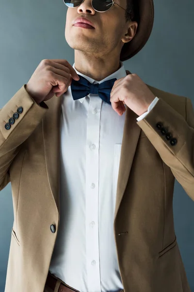 Partial view of stylish mixed race man in suit adjusting bow tie isolated on grey — Stock Photo