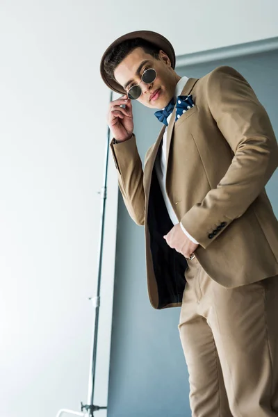 Fashionable mixed race man in suit and hat looking at camera while posing on grey — Stock Photo