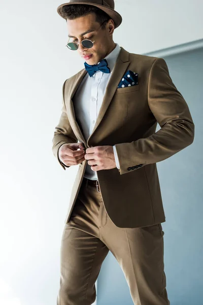 Stilvoller Mixed Race Mann mit Sonnenbrille und Hut im Anzug auf grau — Stockfoto
