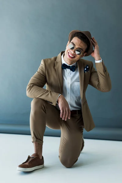 Stylish mixed race man in suit and sunglasses smiling on grey and white — Stock Photo