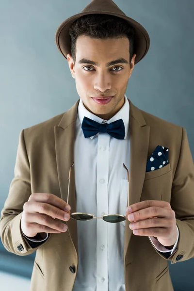 Élégant mixte homme en costume et noeud papillon regardant caméra sur gris — Photo de stock