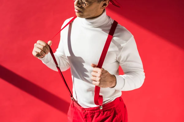 Vista cortada do homem de raça mista na moda em suspensórios posando no vermelho — Fotografia de Stock