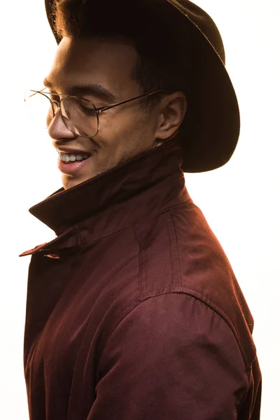 Elegante hombre de raza mixta en gafas y sombrero sonriendo y posando aislado en blanco - foto de stock