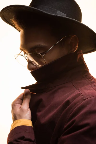 Élégant mixte homme de race dans des lunettes et chapeau posant isolé sur blanc avec la lumière du soleil — Photo de stock