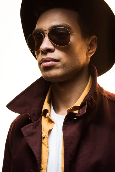 Elegante hombre de raza mixta en gafas de sol y sombrero posando aislado en blanco - foto de stock