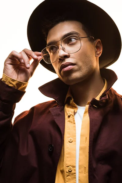 Élégant homme de race mixte dans le chapeau tenant des lunettes et posant isolé sur blanc — Photo de stock