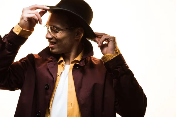 Elegante hombre de raza mixta en gafas de ponerse el sombrero aislado en blanco con espacio de copia - foto de stock