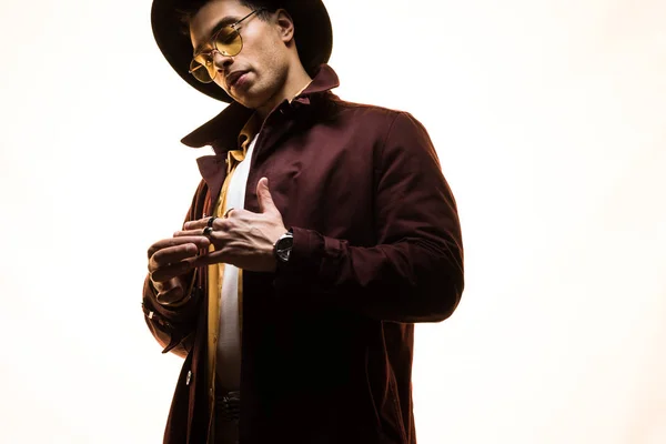 Stylish mixed race man in glasses and hat putting on rings on white with copy space — Stock Photo