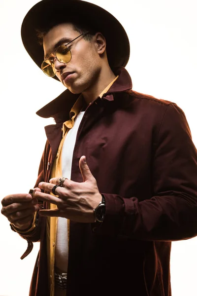 Fashionable mixed race man in hat and sunglasses putting on rings isolated on white — Stock Photo