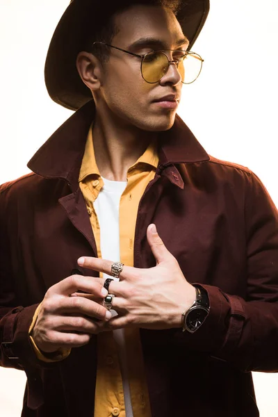 Stylish mixed race man in hat and sunglasses putting on rings isolated on white — Stock Photo