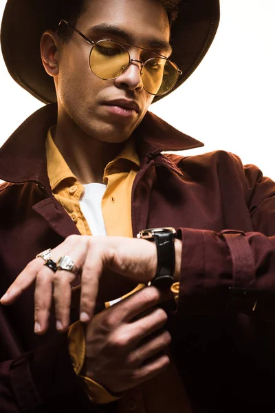 Stylish mixed race man in hat and sunglasses putting on watch isolated on white — Stock Photo