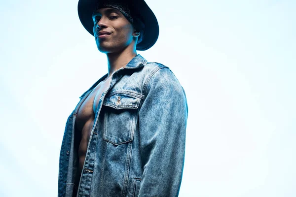Bonito elegante misto raça homem em jeans e chapéu posando isolado em azul com espaço de cópia — Fotografia de Stock