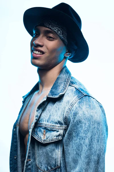 Handsome stylish mixed race man in denim and hat posing and smiling isolated on white — Stock Photo