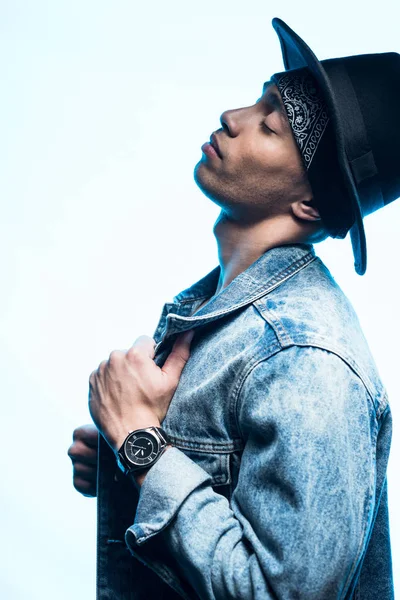 Side view of handsome stylish mixed race man in denim and hat posing isolated on blue — Stock Photo