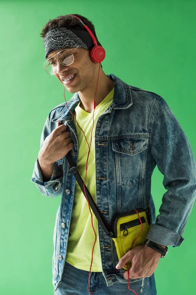 Schöner gemischter Mann mit Kopfhörern, der Musik hört und auf grünem Bildschirm lächelt — Stockfoto