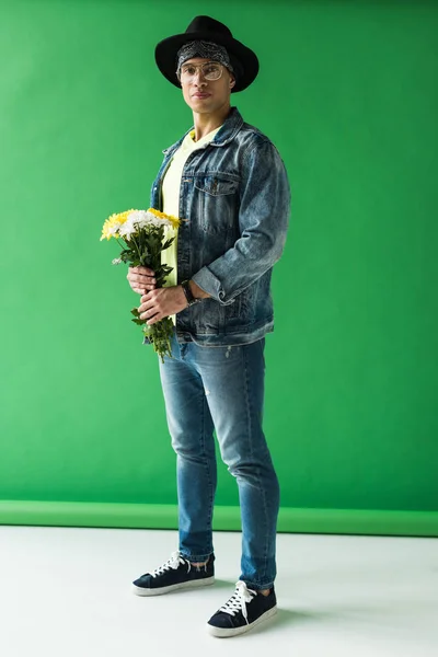 Стильний змішаний гоночний чоловік тримає квіти і дивиться на камеру на зеленому — стокове фото