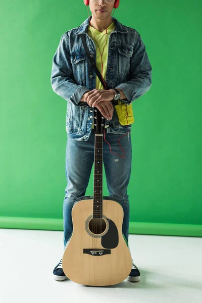 Cropped view of mixed race man in denim posing with acoustic guitar on green — Stock Photo