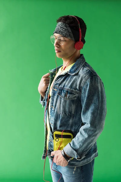 Schöner gemischter Rassenmann mit Kopfhörern und Jeans, der Musik auf grünem Bildschirm hört — Stockfoto