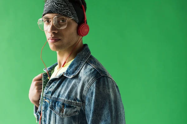 Handsome mixed race man in headphones looking at camera while listening music on green screen with copy space — Stock Photo