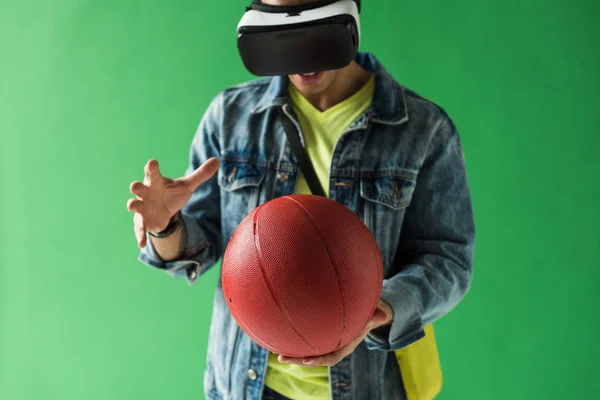 Hombre de raza mixta en los auriculares de realidad virtual gesto mientras sostiene el baloncesto en la pantalla verde - foto de stock