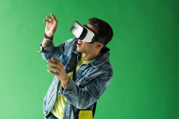 Homem de raça mista surpreso em vr gesto headset enquanto experimentando realidade virtual na tela verde — Fotografia de Stock