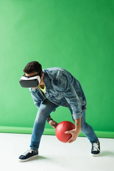 Homem de raça mista em realidade virtual headset segurando basquete em verde com espaço de cópia — Fotografia de Stock