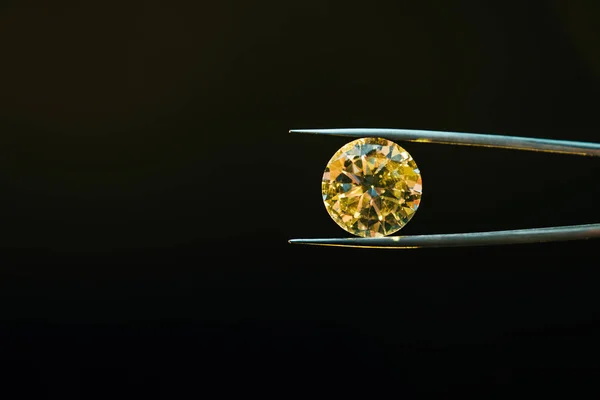 Colorful yellow sparkling diamond in tweezers isolated on black — Stock Photo